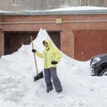 Cheerful girl with the shovel for snow removal stands near a huge snowdrift near the garage Royalty Free Stock Photo