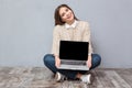 Cheerful girl sitting on floor and holding blank laptop screen Royalty Free Stock Photo