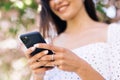 Cheerful girl with smartphone in park on a background of sakura trees. Smiling lady holding cellphone in hands outside