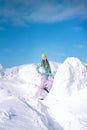 Cheerful girl snowboarder in blue sweater in front of snowy mountains