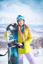 Cheerful girl snowboarder in green jacket in front of peaks snowy volcanos