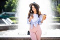 Cheerful girl in the street drinking morning coffee and use her smartphone. Young woman using phone on the street. Woman texting Royalty Free Stock Photo