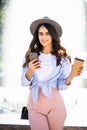 Cheerful girl in the street drinking morning coffee and use her smartphone. Young woman using phone on the street. Woman texting Royalty Free Stock Photo