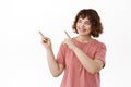 Cheerful girl student with curly hairstyle, pointing and looking at upper left corner with pleased white smile, happy Royalty Free Stock Photo