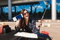 Cheerful girl in sunglasses with map leaning on cabriolet car while happily taking photos on cellphone with passport in Royalty Free Stock Photo