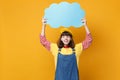 Cheerful girl teenager in french beret, denim sundress hold blue empty blank Say cloud, speech bubble isolated on yellow Royalty Free Stock Photo