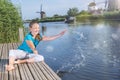 Cheerful girl  tourist splashing in the river on the beautiful landscape backgorund with old windmills in Netherlands Royalty Free Stock Photo