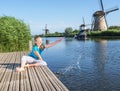 Cheerful girl  tourist splashing in the river on the beautiful landscape backgorund with old windmills in Netherlands Royalty Free Stock Photo