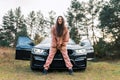 Cheerful girl in tracksuit stands in front of the car.