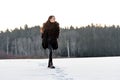 a cheerful girl in a warm fur coat walks across the open field leaving footpath in the snow