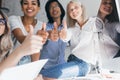 Cheerful girl in white blouse and blue jeans sits on table and posing with international friends. Asian young man and