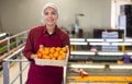 Cheerful girl worker with box of tangerines at fruit sorting factory