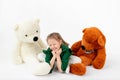 A cheerful girl of 8 years old sits among toys of bears on a white background, space for text