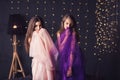 Cheerful girlfriends. Two long-haired girls in pink and purple dresses in studio on dark background with bokeh. Copy space. Royalty Free Stock Photo