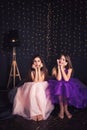 Cheerful girlfriends. Two long-haired girls in pink and purple dresses in studio on dark background with bokeh. Copy space.