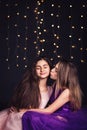 Cheerful girlfriends. Two long-haired girls in pink and purple dresses in studio on dark background with bokeh. Copy space. Royalty Free Stock Photo