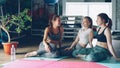 Cheerful girls are socialising in wellness center sitting on yoga mats on wooden floor. Sports equipment, green plant Royalty Free Stock Photo