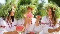 Cheerful girls in floral circlets eating watermelons outside in summer