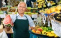 Positive senior male owner of greengrocery shop in apron offering fresh fruits and vegetables Royalty Free Stock Photo