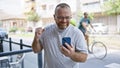 Cheerful, glasses-wearing, bearded, middle-aged caucasian man grooving to music blaring from his phone on a lively, urban street