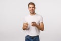 Cheerful good-looking modern blond man with bristle, holding paper cup of coffee, drinking tea and holding smartphone