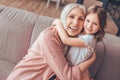 Cheerful grandmother hugging granddaughter sitting on the sofa in living room and looking at the camera Royalty Free Stock Photo