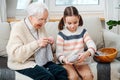 Cheerful granny knitting on a couch at home, her granddaughter helping her
