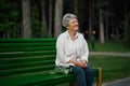 Cheerful granny leisures on bench in summer park