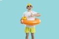 Cheerful guy with funny inflatable circle for swimming shows thumb up on light blue background.