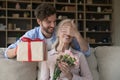 Cheerful guy giving surprise gift to old senior mom Royalty Free Stock Photo