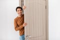 Cheerful guy looking out of door standing in doorway