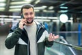 Cheerful guy talking on phone near escalator at subway station Royalty Free Stock Photo