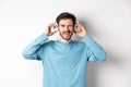 Cheerful guy wink at camera and smiling, listening music in wireless headphones, white background Royalty Free Stock Photo