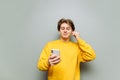 Cheerful guy in yellow clothes uses a smartphone on a gray background and listens to music in headphones with a smile on his face Royalty Free Stock Photo