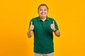 Cheerful handsome asian young man showing thumbs up gesture isolated on yellow background