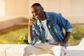Cheerful handsome black guy sitting on street, talking on phone Royalty Free Stock Photo