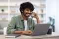 Cheerful handsome indian guy working online, having phone conversation Royalty Free Stock Photo