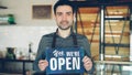 Cheerful handsome man small coffee-house owner is holding We Are Open sign while standing inside coffee shop. Opening Royalty Free Stock Photo