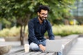 Cheerful millennial indian guy freelancer working on street, using laptop Royalty Free Stock Photo