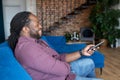 Cheerful and happy African-American man with dreadlocks holding TV remote controller Royalty Free Stock Photo