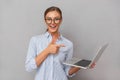 Cheerful happy business young woman posing isolated over grey wall background using laptop computer pointing.