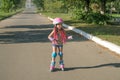 A cheerful happy child in a sports protective helmet and knee pads is skating on an asphalt path in the suburbs.