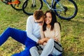 Cheerful and happy couple is laughing and hugging when sitting on a green lawn in the city park. Their bicycles are on the Royalty Free Stock Photo