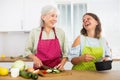 Happy elderly mother and her daughter prepare vegetable salad and have delicious lunch in the kitchen Royalty Free Stock Photo