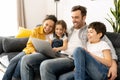 Cheerful happy family of four using laptop sitting on the sofa in cozy apartment Royalty Free Stock Photo