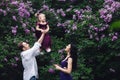 Cheerful happy family near lilac flowering bushes. dad throws up little daughter up Royalty Free Stock Photo