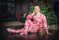Cheerful happy funny man in pink sleepwear sitting on the floor near decorated fir tree Royalty Free Stock Photo