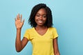 Cheerful happy girl in stylish yellow T-shirt with raised arm greeting somebody