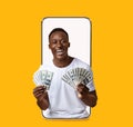 Cheerful happy glad young handsome black man show many dollars on empty screen of large phone
