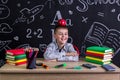 Cheerful and happy hellion schoolboy sitting at the desk with books, school supplies, with a red apple on the top of his